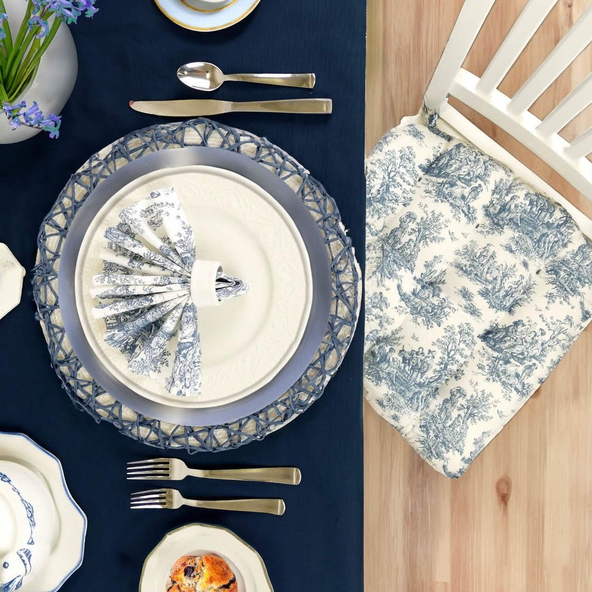 Elegant table setting toile chair cushion, and blue and white china on a blue tablecloth.