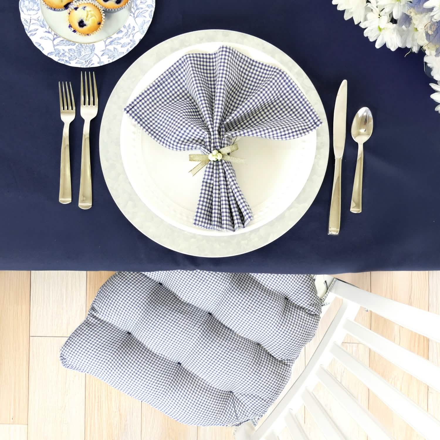 Table setting with a checkered napkin on a white plate, silverware, and a blue tablecloth.