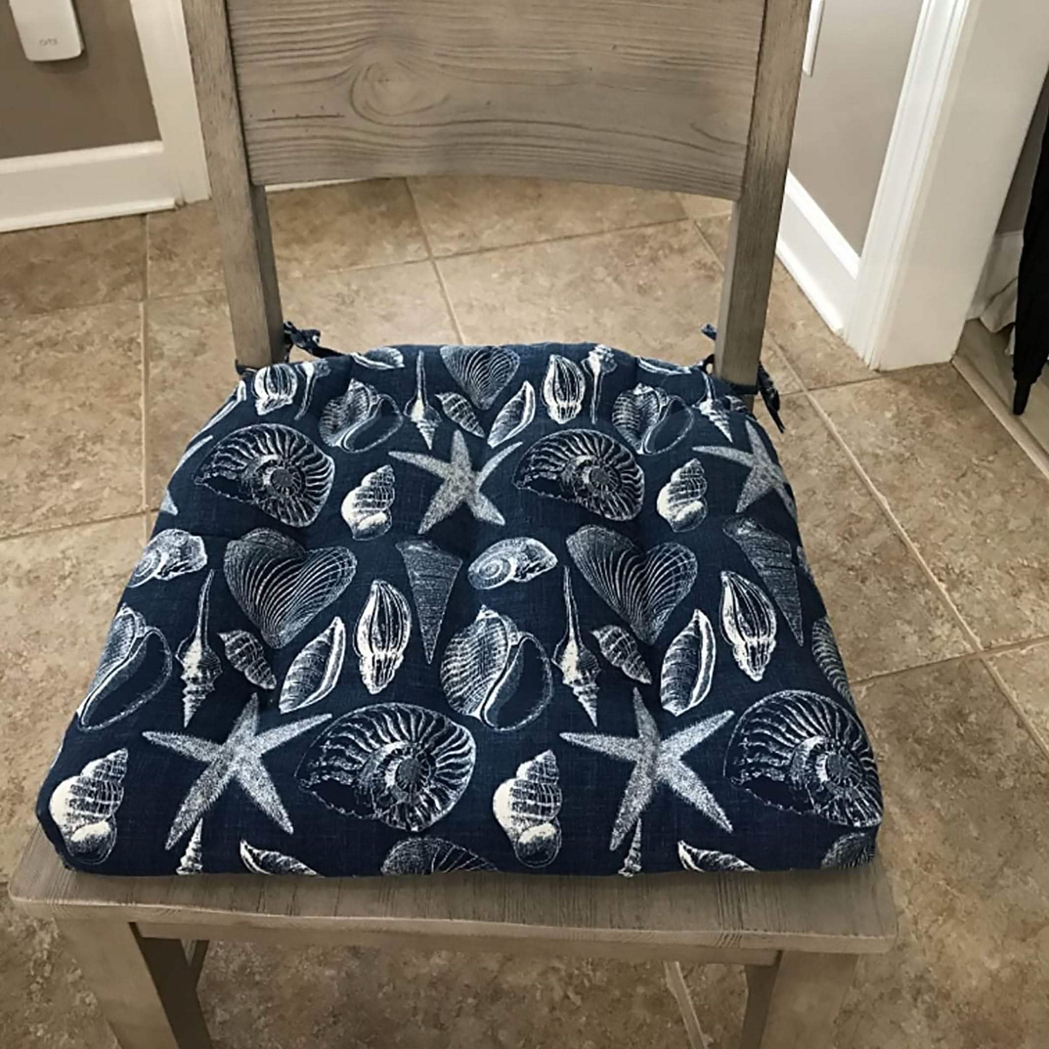navy blue outdoor dining chair cushion with coastal seashell design arranged on dining room chair