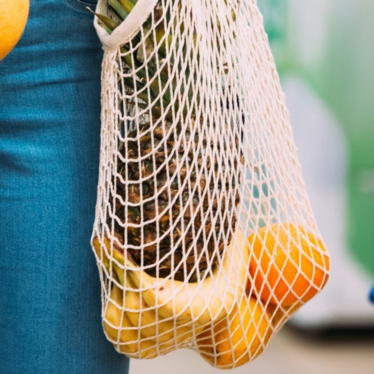 Person holding a mesh bag with oranges and an orange in their hand.