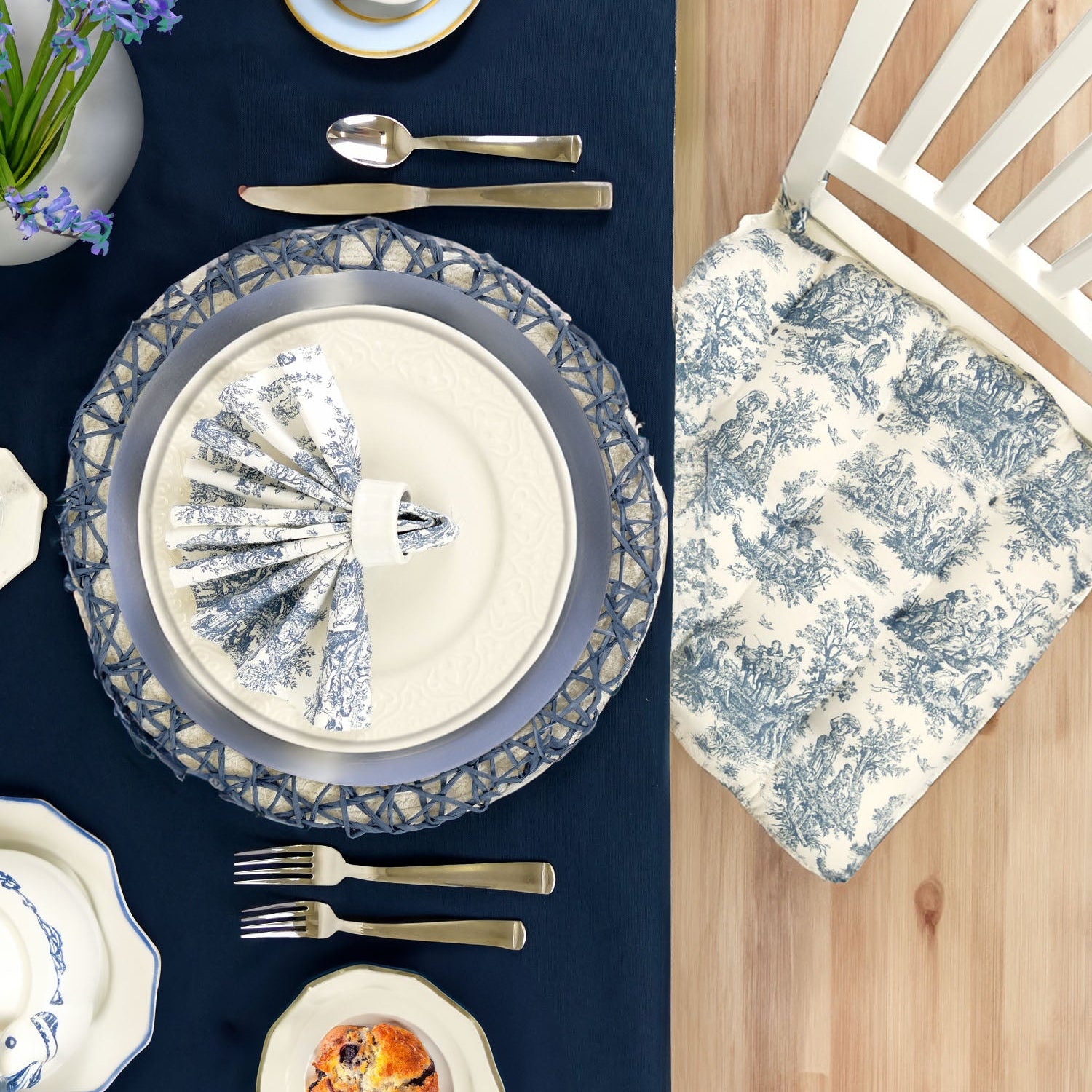 Elegant table setting toile chair cushion, and blue and white china on a blue tablecloth.