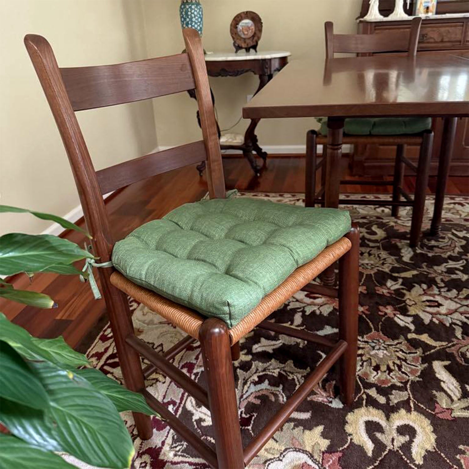 Wooden chair with a green cushion on a patterned rug in a room with a dining table.